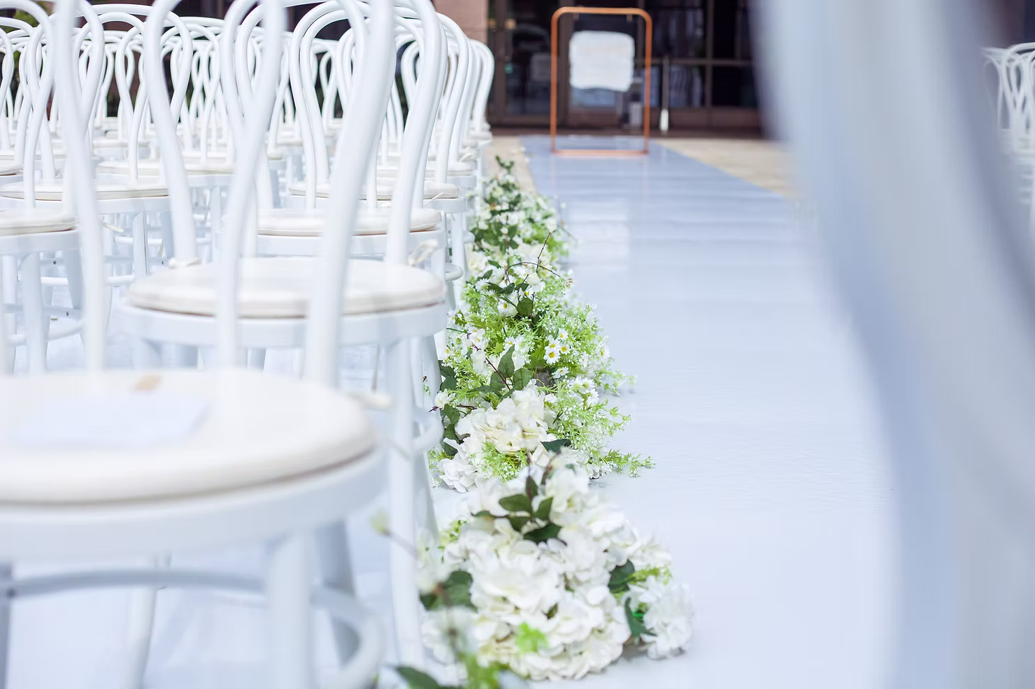 White chairs and floral aisle décor prepared for a wedding ceremony